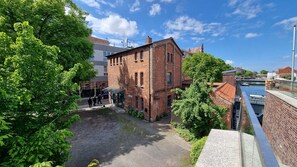A courtyard with a brick building, a covered walkway, and a canal with a boat. - Fewo 1 im Alten Zollhaus Stralsund - Holiday apartment 1 in the old customs house directly at the (Stralsund)