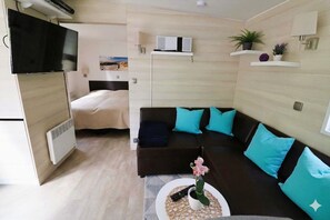 Ein kleiner Wohnraum mit Bett, einer Couch, einem Fernseher und einem Tisch mit Pflanze.