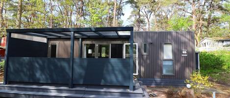 A modern, two-story cabin with a dark exterior, large windows, and a covered outdoor area.