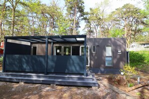 Eine moderne, zweistöckige Holzhütte mit dunkler Fassade, großen Fenstern und einer überdachten Terrasse.