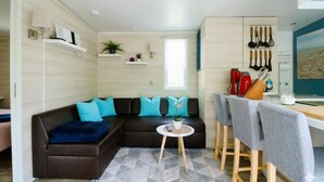 Ett kompakt bostadsutrymme med en soffa, ett litet runt bord, en matplats med stolar, ett kök med köksredskap och ett fönster.