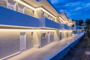 A modern hotel with a long corridor, multiple doors, and a covered outdoor seating area. - SolMare Deluxe Suites (Mastihari)