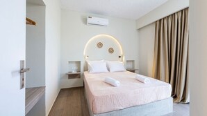 Quarto de hotel com cama, ar-condicionado fixado na parede, mesa de cabeceira e cortina.