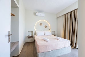 A hotel room with a bed, a wall-mounted air conditioner, a bedside table, and a curtain. - SolMare Deluxe Suites (Mastihari)
