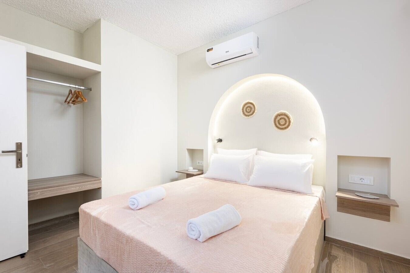 A hotel room with a bed, a wardrobe, an air conditioning unit, and a bedside table.