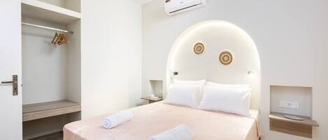 A hotel room with a bed, a wardrobe, an air conditioning unit, and a bedside table.