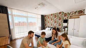 Uma família jogando um jogo de tabuleiro em um quarto com uma cama, um guarda-roupa e uma janela com cortinas.