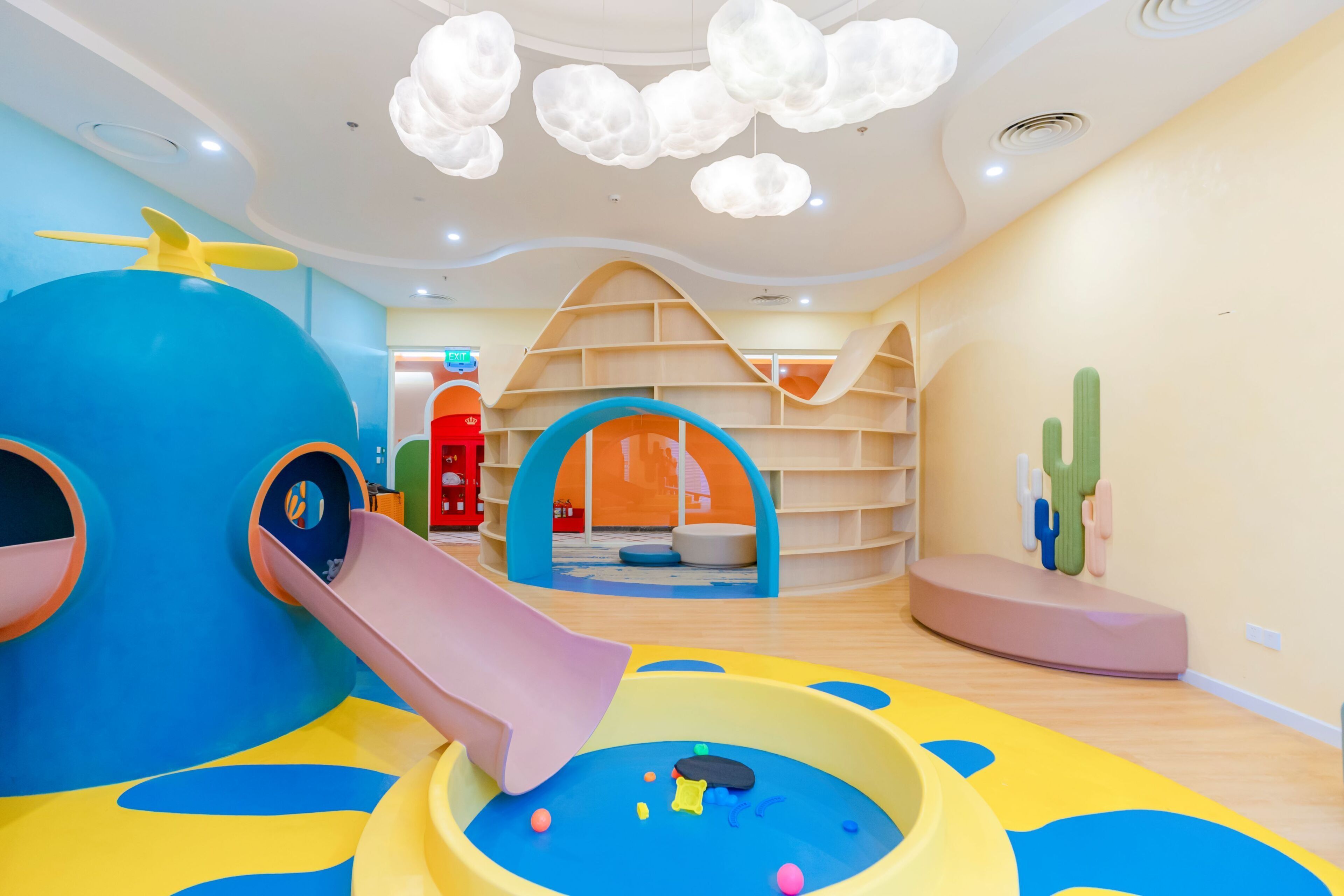 Uma área de recreação infantil com escorrega, mesa de bilhar e uma decoração de cactos.