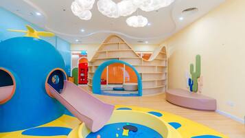Uma área de recreação infantil com escorrega, mesa de bilhar e uma decoração de cactos.