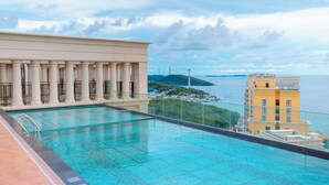 A rooftop pool with a view of the sea and a building with columns. - Dido Carthage Apartment (An Thoi)