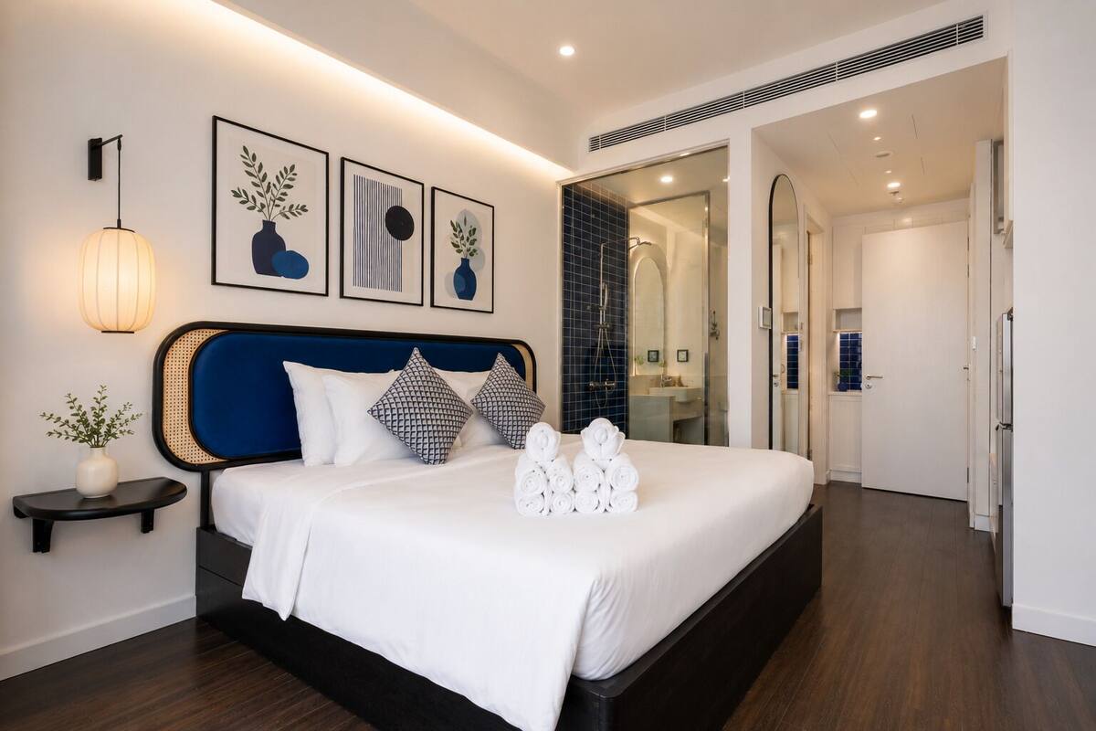 Una habitación de hotel moderna con una cama grande, una mesita de noche con un florero y obras de arte enmarcadas en la pared.