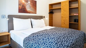 Een slaapkamer met een bed, een nachtkastje, een houten garderobe en een aan de muur hangend schilderij.