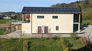 Een modern huis met een dakbedekt met zonnepanelen, een overdekt terras en een kleine tuin.