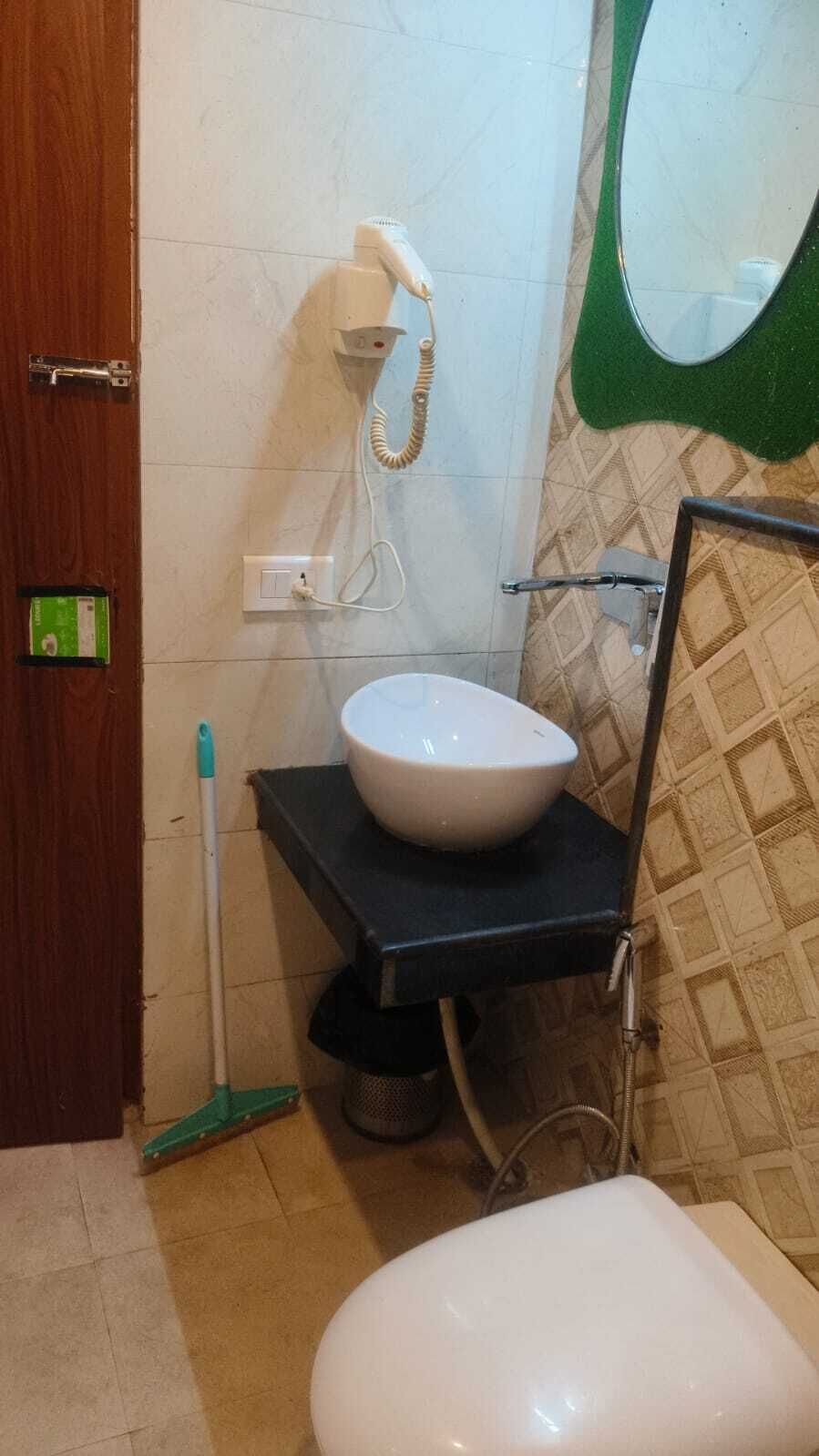 A bathroom with a white sink, a green floor mat, a mop, and a shower area.