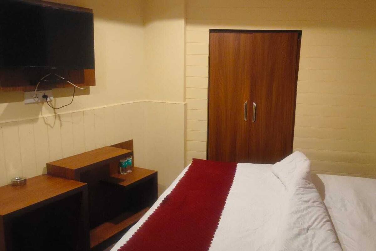 A bedroom with a bed, a wooden nightstand, a television mounted on the wall, and a wooden door.
