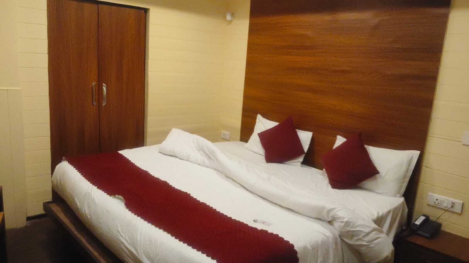 A hotel room with a bed, wooden wardrobe, and a wooden headboard.