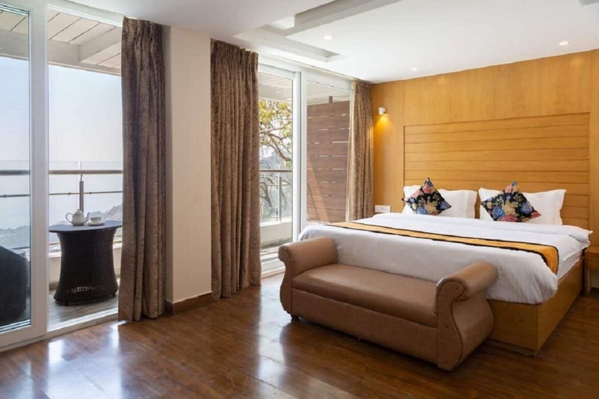 A bedroom with a bed, a bench, a table with a cup, and a view through a glass door.