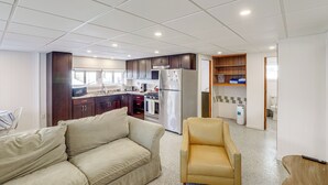 Una sala de estar con sofá y sillón, una cocina con armarios oscuros y electrodomésticos de acero inoxidable, y un salpicadero de azulejos.