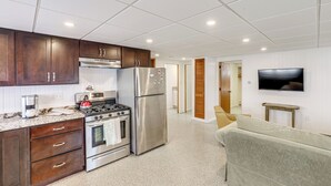 Una cocina moderna con armarios de madera, electrodomésticos de acero inoxidable, un televisor de pantalla plana y un sofá en la sala.