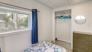 Un dormitorio con cama, cómoda, ventana con cortinas, armario con estantes y espejo en la pared.