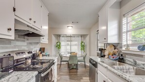 Une cuisine moderne avec des meubles blancs, une cuisinière, un lave-vaisselle et un coin repas comprenant une table et des chaises.