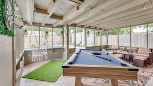 Une table de billard dans un espace extérieur abrité, avec un fauteuil suspendu et un ensemble de mobilier de salle à manger.