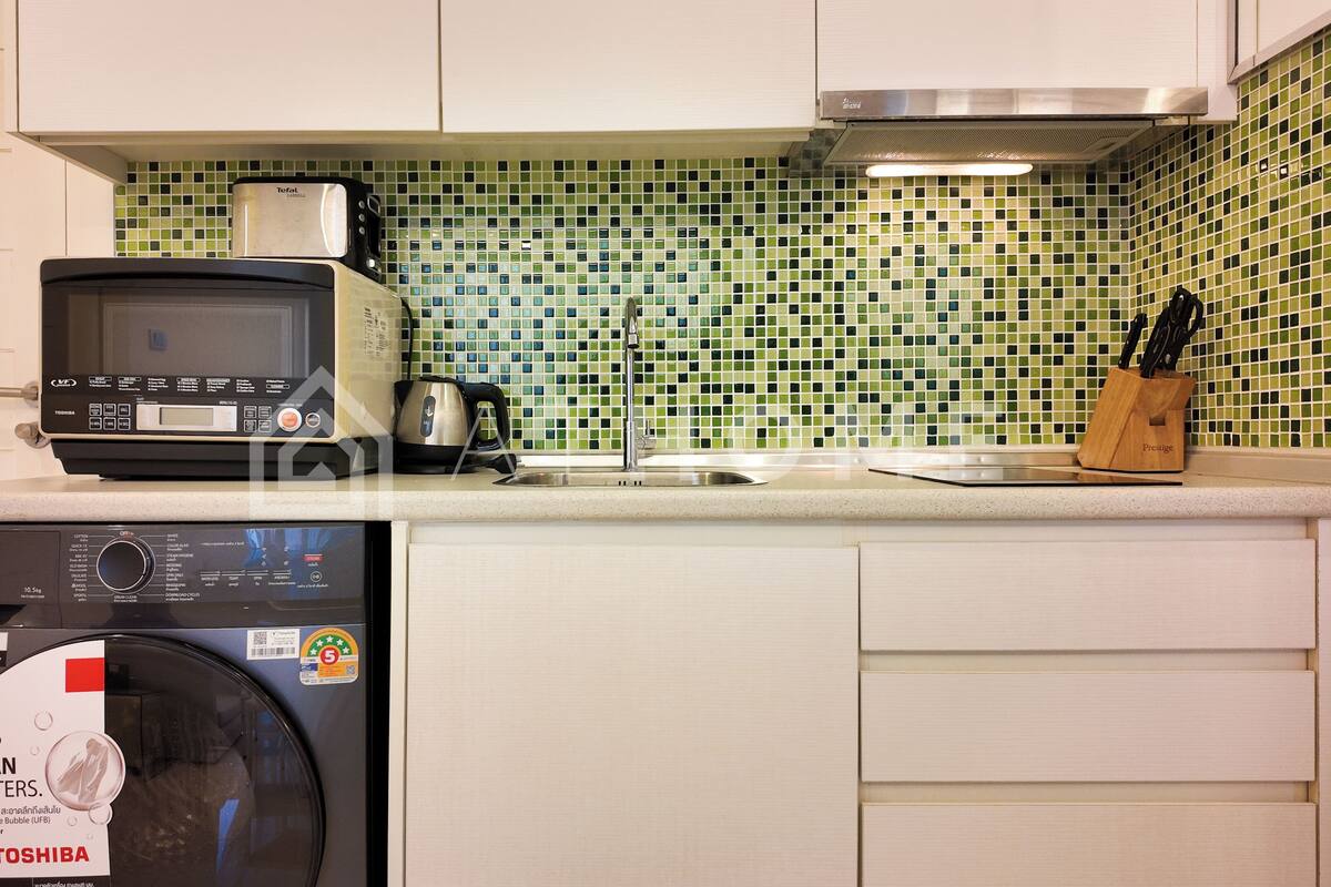 A kitchen with a washing machine, a toaster, and a knife block on the counter.