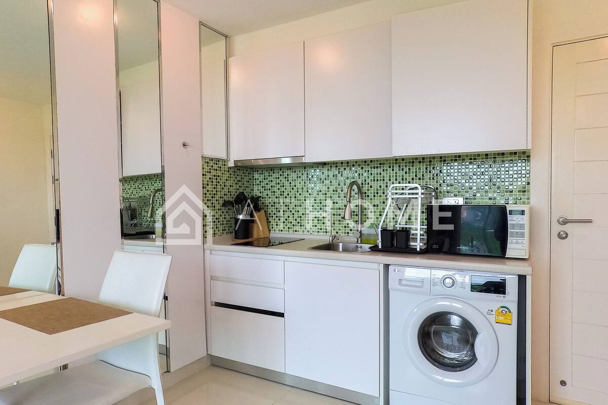 A modern kitchen with white cabinets, a washing machine, a microwave, and a sink.
