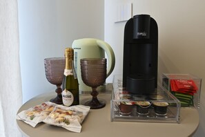 Een tafel met een fles Maschio Prosecco, twee glazen, een koffiezetapparaat en verpakte snacks.
