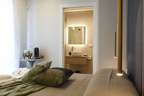 Een hotelkamer met een bed, een nachtkastje met een fles en glazen, een klein tafeltje met een fles en glazen, een spiegel en een wastafel.