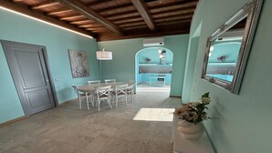 Una habitación con comedor, una mesa blanca con sillas, una consola blanca con un jarrón y un espejo en la pared.