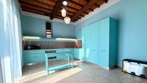 Una cocina con gabinetes color turquesa, encimera de granito, campana extractora de acero inoxidable y una lámpara colgante.