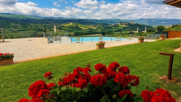 Una piscina con sillas de descanso, un área con césped y vistas a colinas ondulantes.