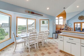 A dining area with a table and chairs, a kitchen with cabinets and a counter, and large windows with a view. - Walk to the Beach! 5BR Outer Banks Home (Kitty Hawk)