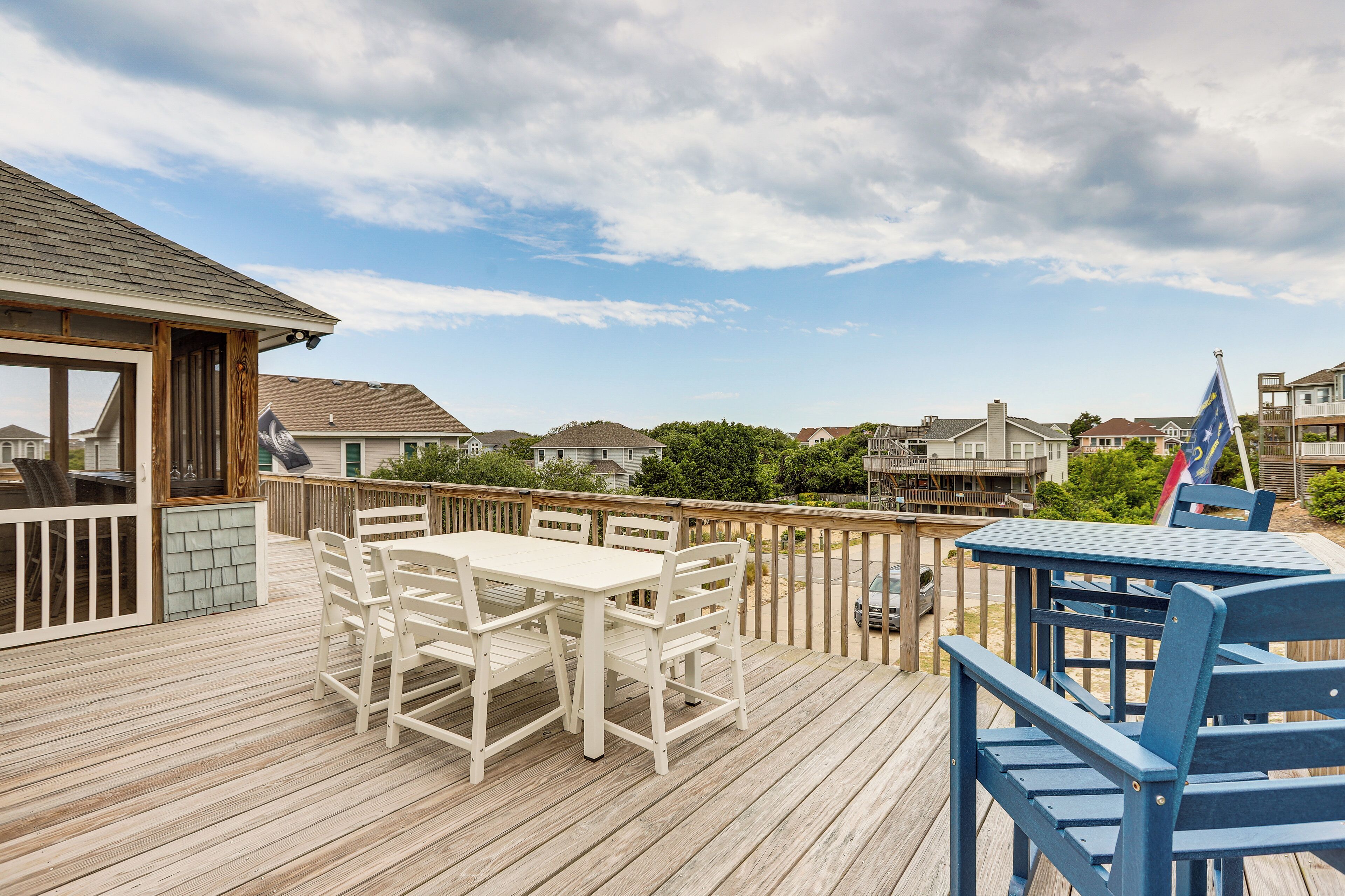 Een houten terras met een tafel, stoelen, een barbecue en een uitzicht op huizen.