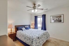 A bedroom with a bed, a ceiling fan, a nightstand, a lamp, a window with curtains, and a framed picture on the wall. - Gateway to Zion NP! Group Getaway w/ Mtn Views (Enoch)