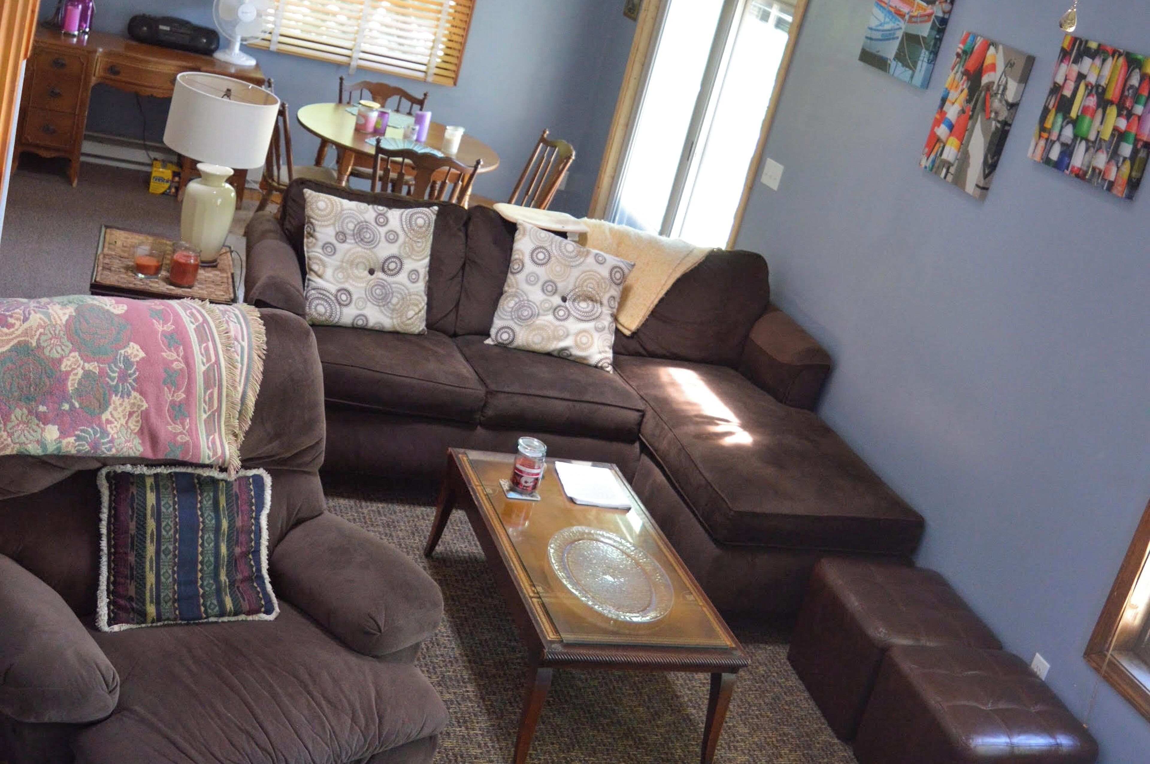 A living room with a brown sofa, a glass coffee table, and a dining area with a table and chairs.