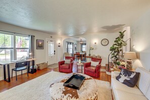 A spacious living room with a large window, a dining area, and a cozy seating area with leather chairs and a white sofa. - Walkable Family Home in the Heart of Kalispell (Kalispell)