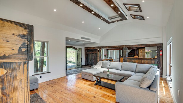 Uma sala de estar ampla com um sofá seccional grande, piso de madeira e um design moderno no teto.