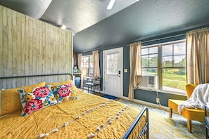 Ein Schlafzimmer mit einem Bett, einem Sessel, einem Schreibtisch und einem Fenster mit Vorhängen.