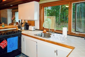 A kitchen with a stove, sink, and window overlooking a wooded area. - 2 Mi to Beaches: Cape Cod Cottage w/ Fire Pit (Truro)