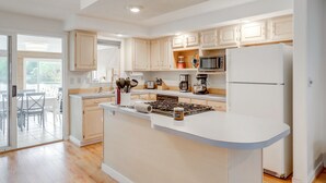A modern kitchen with white cabinets, a central island, and a refrigerator. - Kayaks, Paddleboat! Lakefront Retreat in Barnstead (Barnstead)