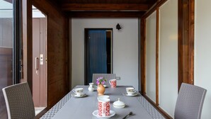 Una mesa de comedor con vajilla blanca y roja estampada, un florero con flores y una cortina azul al fondo.