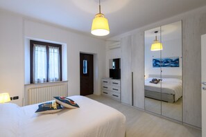 Ein Schlafzimmer mit einem Bett, einem Schminktisch, einem Fernseher, einem Spiegel und einem Fenster.