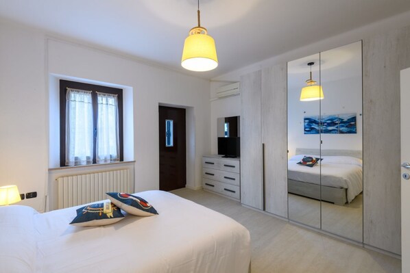 Ein Schlafzimmer mit einem Bett, einem Schminktisch, einem Fernseher, einem Spiegel und einem Fenster.