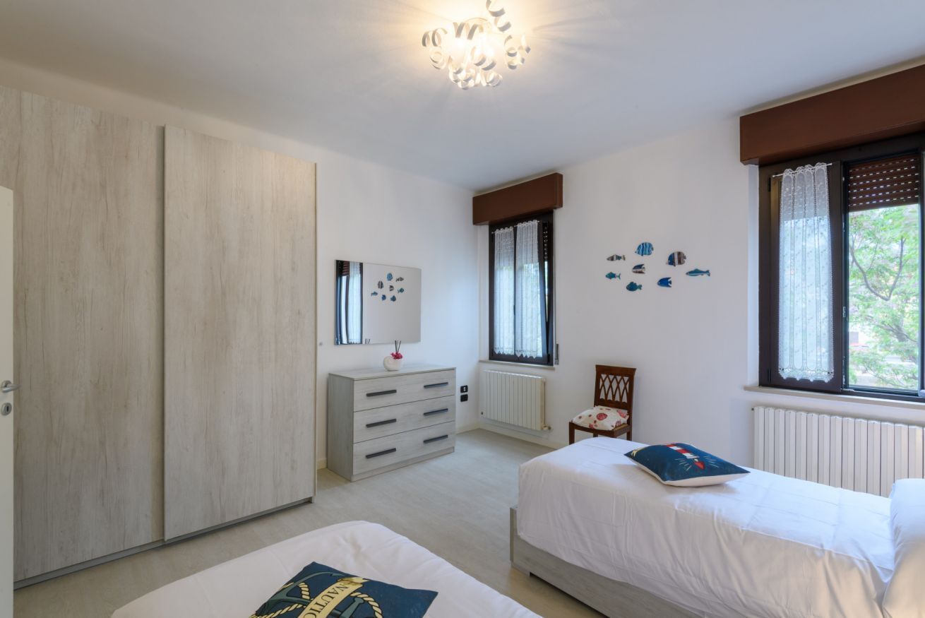 A bedroom with two beds, a dresser, a radiator, and a window with curtains.