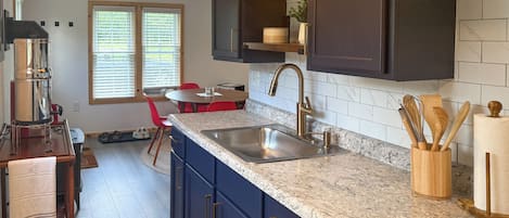 A kitchen with dark cabinets, a granite countertop, a stainless steel sink, and a red chair.