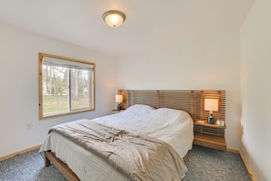Ein Schlafzimmer mit Bett, Fenster, Nachttisch mit Lampe und Deckenleuchte.