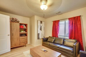 Een woonkamer met een houten kast, een leren bank, een salontafel en een raam met rode gordijnen.