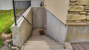 Un escalier en béton avec une rampe métallique, menant à une porte sur laquelle est fixée une applique lumineuse.